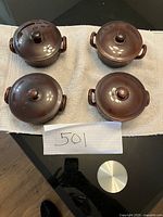 Top down view of four clay pots with lids arranged in a square, showing round shape, handles and dark brown glossy lids.