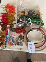 Overview of crewel embroidery materials including skeins of yarn, embroidery hoops, and packaged kits laid out on a white surface.