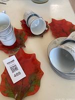 4 large glass oak leaf shaped decorative plates in red and green hues, some cups placed on top.