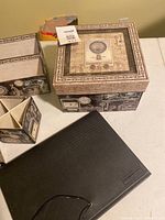 Set of desk organizer boxes with vintage style prints and a closed black file folder on a white table.