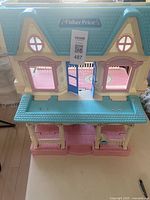 Front view of Fisher Price plastic dollhouse showing double blue doors, pink porch with columns, and two upper floor windows.