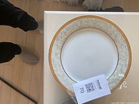 White china dinner plate with intricate gold patterned rim on a flat plate.