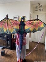 Front view of colorful large dragon kite held by person inside a home, shows full wingspan and tail.