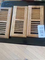 Photo of 3 oak floor vents arranged side by side on a dark surface showing their wood grain and slats.