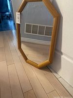 Full view of the octagonal oak framed mirror standing against a white wall, showing its frame design and reflective surface.