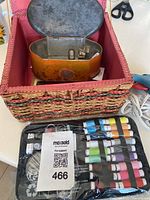 Lot showing wicker sewing box, sewing threads, hot glue tool, scissors, framed bird picture, and keychain on table.