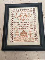 Close-up photo of framed needlepoint wall hanging showing the detailed stitching and text.