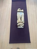 Purple yoga mat laid out flat on wooden floor, with beige carrying case placed on top near one end.
