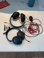 Photo showing two headsets on a table: one black Beats headphone with taped headband and cables, and a black Bose headset without cables.