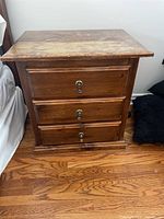 Front view of solid wood bedside table with three drawers and metal keyhole hardware.