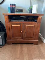 Front view of medium wood cabinet showing two-door compartment and open shelf above.