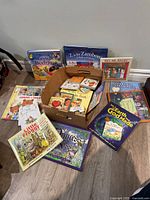 Overview of children's books spread out on floor including both religious and classic titles, some hardcover, some paperback.