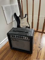 Full lot shot showing guitar leaning against banister and amplifier in front on hardwood floor