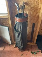 Full view of black golf bag with brown leather trim containing golf clubs