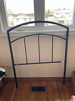 Front view of black metal bed headboard against window, showing curved top and vertical bars.