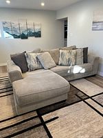 Front three-quarter view of sectional sofa with chaise in a basement room, showing seat cushions, back cushions and throw pillows.