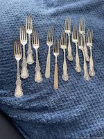 Nine silver plated forks laid on dark blue textured fabric. Four forks on left side stamped J Welsh & Son, four on right side stamped Rogers Bros 126 but unmarked in this photo and show wear, one plain fork in center stamped Henry C Weber.