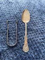 Spoon and sugar tongs laid flat showing details and condition.