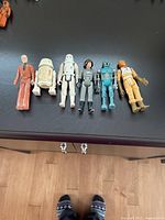 Photo showing six original Star Wars action figures laid out horizontally on a dark surface, including Obi-Wan Kenobi, R2-D2, Snowtrooper, Imperial Officer, IG-88, and Rebel Pilot.