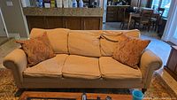 Front view of beige Ethan Allen couch with three seat cushions and two paisley accent pillows, placed in living room.