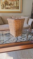 Closed view of large woven basket hamper with solid wooden lid on glass table.