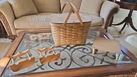 Woven picnic basket with accessories on glass table: two wooden knife blocks with handles and a small folding wooden stand.