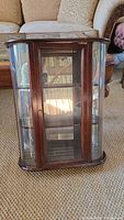 Front view of wood curio cabinet showing glass paneled door, brass knob, and interior shelves