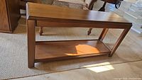 Front and side view of wooden console table showing top surface and bottom shelf on a carpeted floor under natural light.