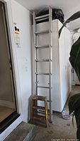 Two ladders side by side, including the taller aluminum extension ladder leaning vertically and the smaller wooden step ladder in front.