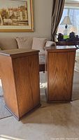 Pair of medium brown wooden storage cabinets with paneled sides and flat tops, photographed indoors near sofa and chairs
