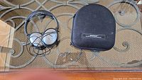 Noise cancelling headphones laid next to a black Bose carrying case on a glass table.