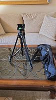 Full view of black tripod set up on glass table with black carrying case beside it