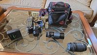 Overall group shot showing camera body, two lenses, strap, bag and battery tester on glass table