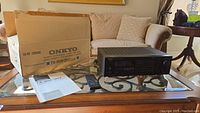 Photo showing Onkyo TX-906 stereo receiver, original box, user manual, and remote control on glass table.