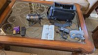 Sony Handycam and accessories on a glass table, showing camera body, case, batteries, remote, manual, adapter, and cables.