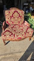 Front view of the vintage red and gold damask upholstered armchair with carved wooden frame.
