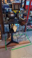 Wide view of bench grinder on stand next to stool and wooden boards