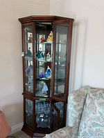 View of entire wood corner curio cabinet filled with collectible figurines. Cabinet has glass panel front door open and glass shelves inside visible.