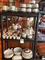 Overall view of stoneware set on black shelving with mugs, saucers, teapot, cream, sugar, and cutlery tray