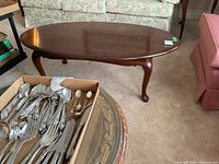 Oval cherry table top with box of silverware in foreground
