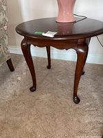Full view of the round cherry wood side table with lamp on top, showing polished wood surface and sculpted legs