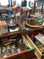 Countertop with assorted utensils including wooden spoons, spatulas, tongs, funnels, digital scale, salt and pepper mills, egg separators, smash burger kit box