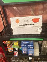Boxed Lagostina Tuscan Collection 4.7L (5QT) oval casserole with cover on a metal shelf, showing front of packaging with branding and product image.