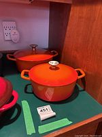 Two orange enameled Dutch ovens on shelf