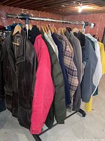 Full view of the metal garment rack loaded with multiple men's jackets including leather, winter, plaid, and rain jackets.