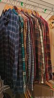 Nine assorted men's long sleeve button-up shirts hanging on wooden hangers showing variety of plaid patterns and colors.