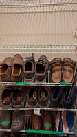 Shelf with 11 men's shoes including tan loafers, dark boots, brown dress shoes, rubber clogs, and athletic sneakers.