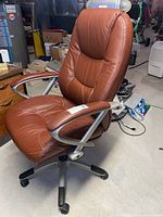Front-right angle view of the high-back tan leather office chair with armrests and five-star caster base