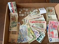 Overview of box with assorted paper money laid flat showing different colors, portraits, and denominations, along with scattered coins mostly silver in color.