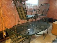 Elliptical green metal mesh table with two chairs placed on top and one next to it showing overall set